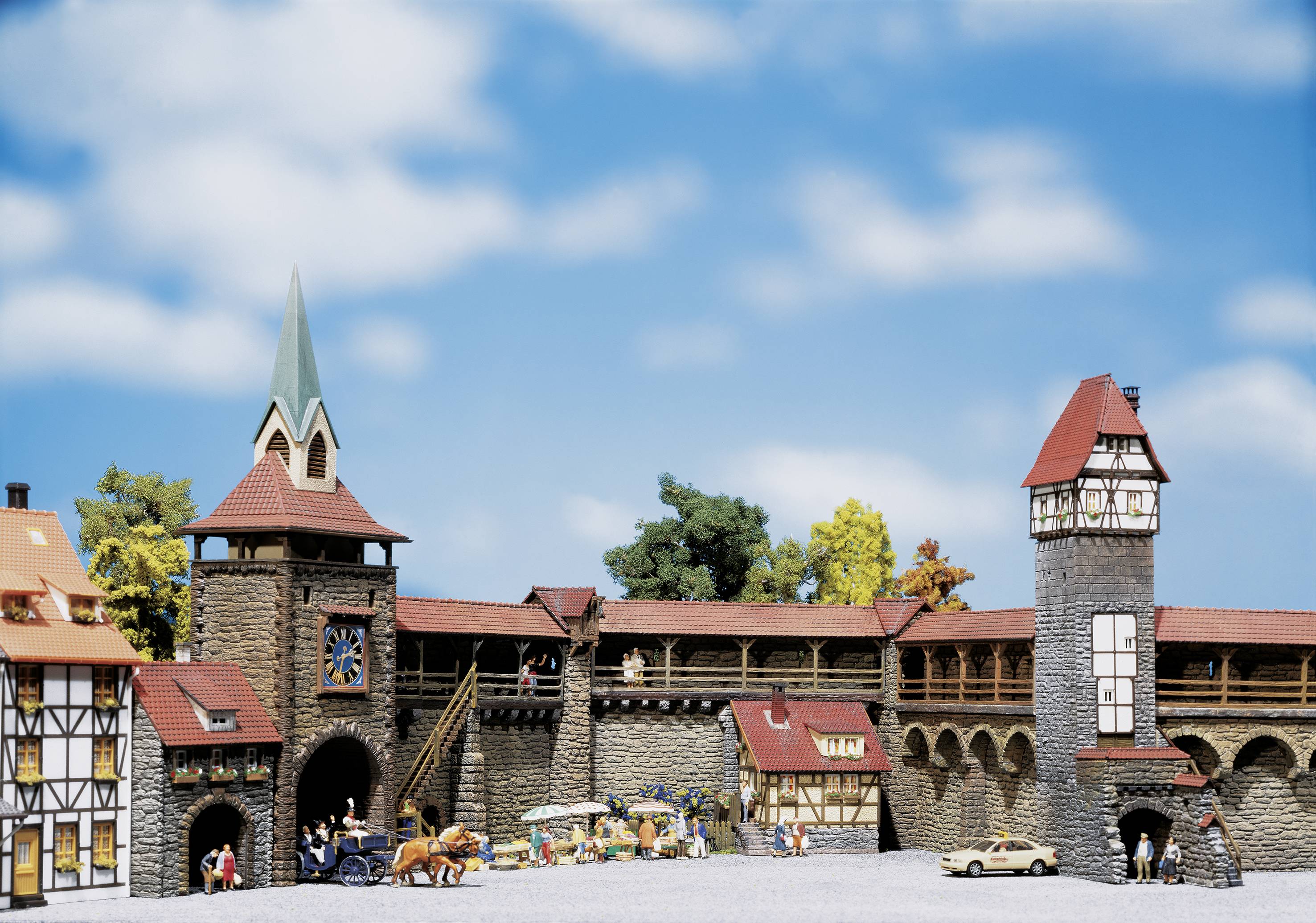 Historic city wall with towers and half-timbered houses beneath a blue sky, brought to life by figures and a horse-drawn carriage in the foreground.