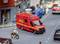 A red toy rescue vehicle with the inscription 'Fire Brigade Rescue' is positioned on a model road, surrounded by miniature vehicles.