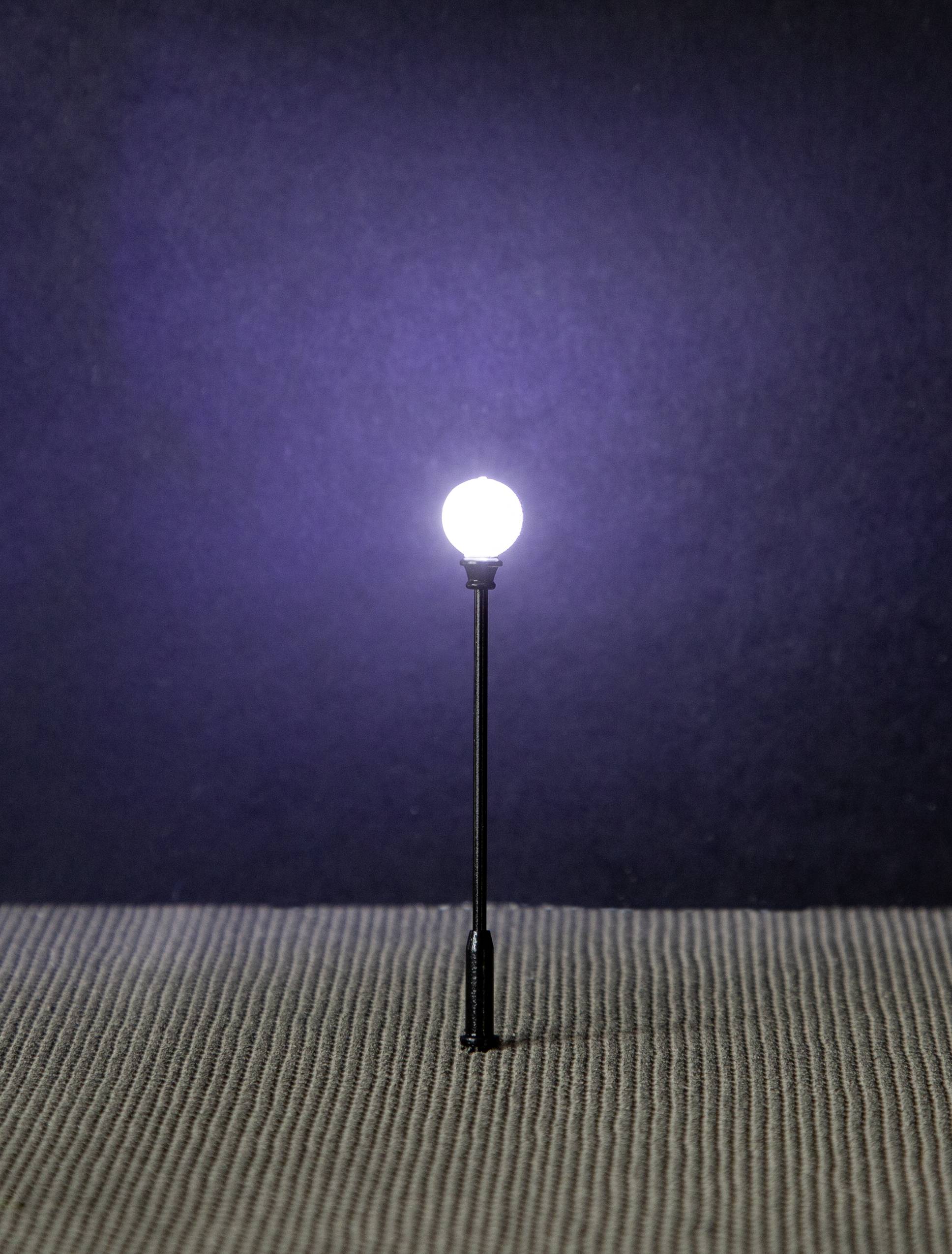 A luminous light bulb on a slender black rod, standing on a ribbed, grey surface, against a dark background.