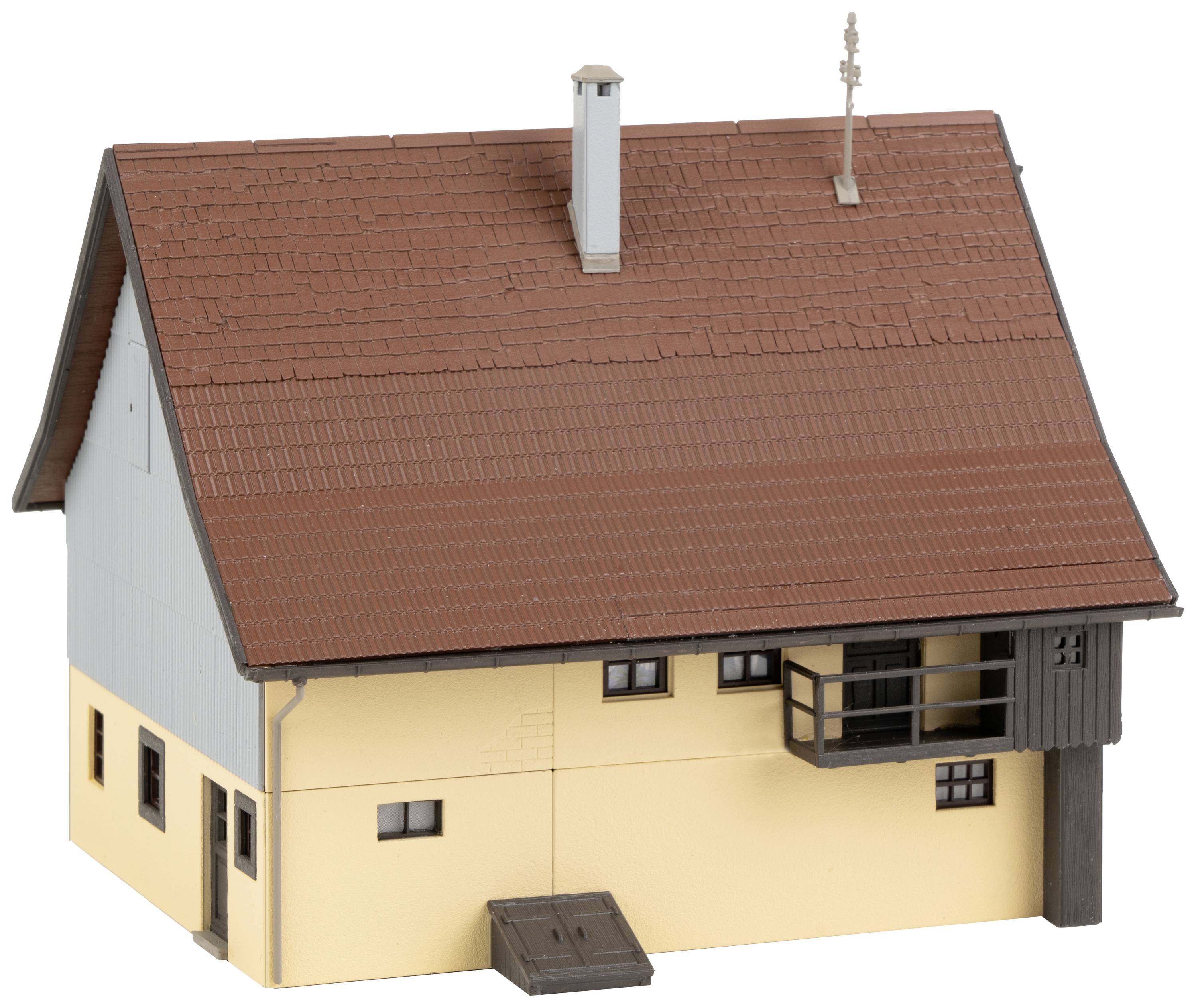 A small, two-storey house with a red pitched roof, yellow render, and several small windows; a balcony protrudes from its facade.