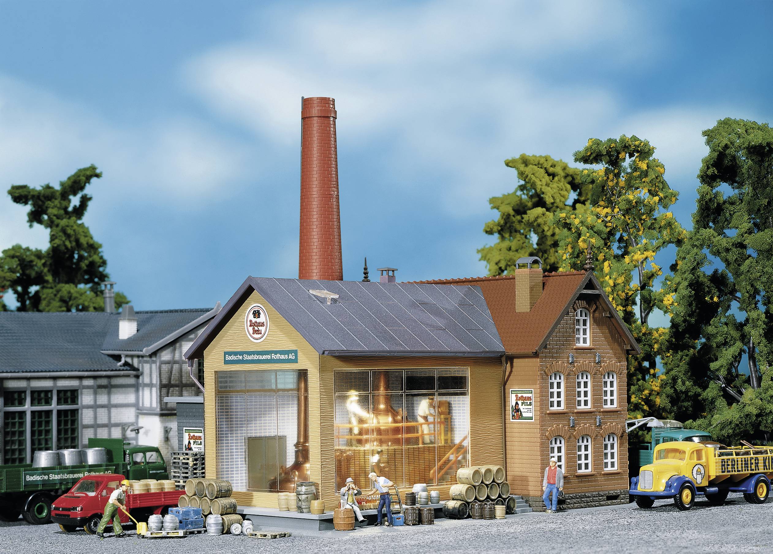 Miniature scene of a brewery with buildings, lorries, and workers transporting barrels. Model depicts a rural brewery setting.