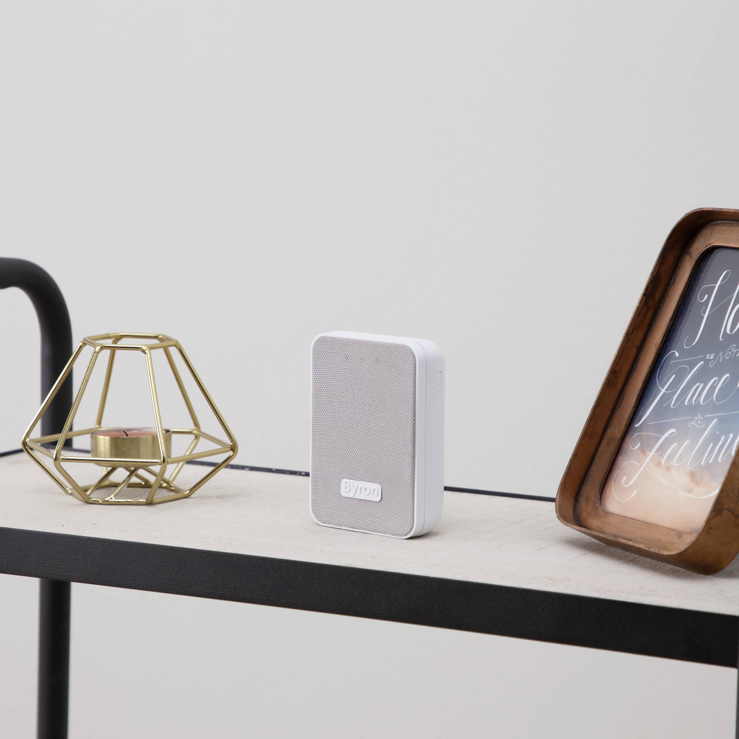 A white, portable speaker sits on a table next to a gold decoration and a framed picture.
