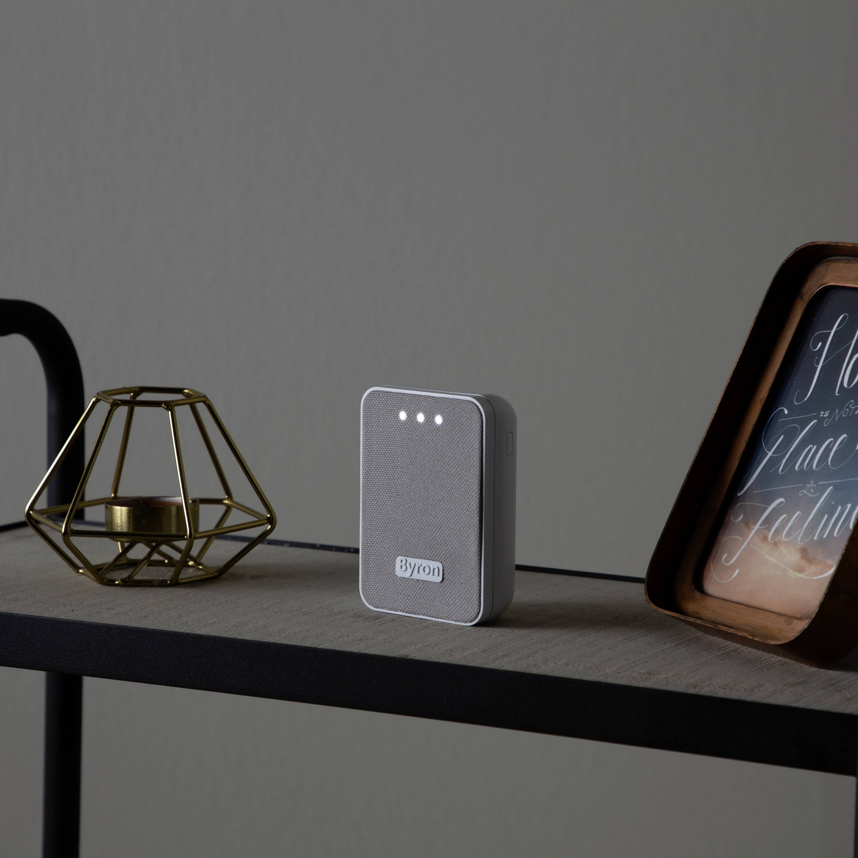A grey Byron door stop stands on a black shelf next to a metal candlestick and a picture frame.