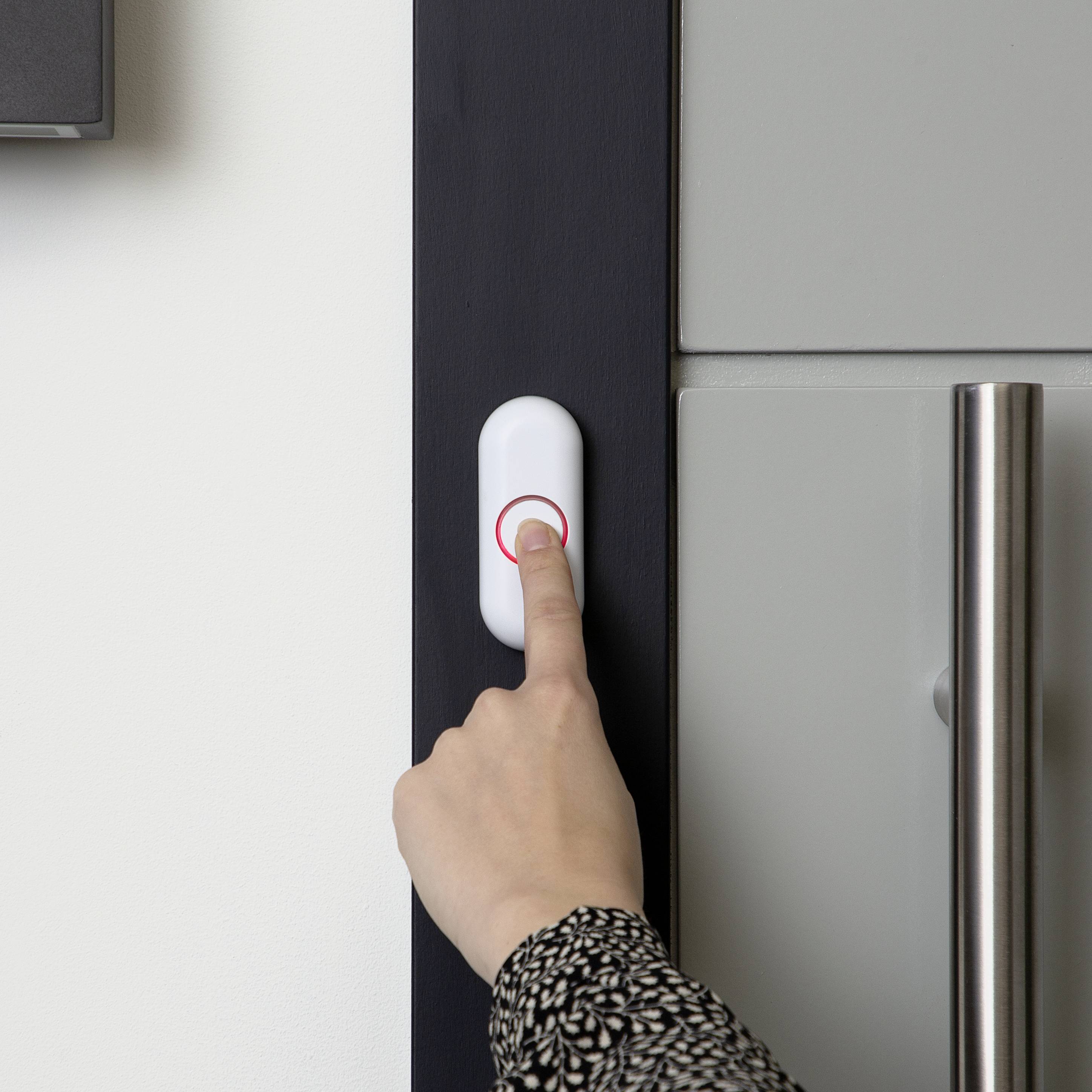 A hand is pressing a doorbell next to a front door with a silver handle. The doorbell has a glowing red rim.