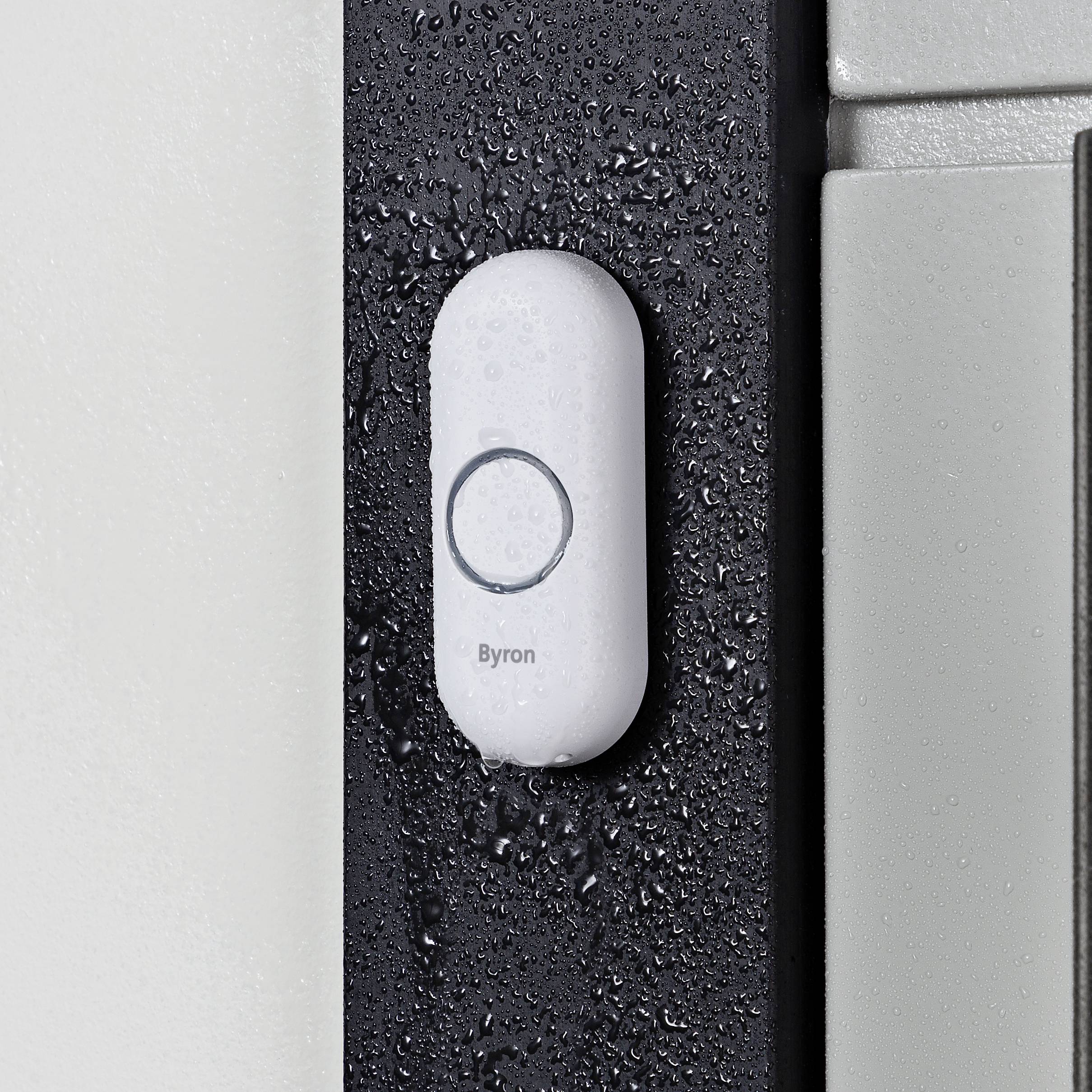 White doorbell with water droplets, mounted on a wall beside a door.