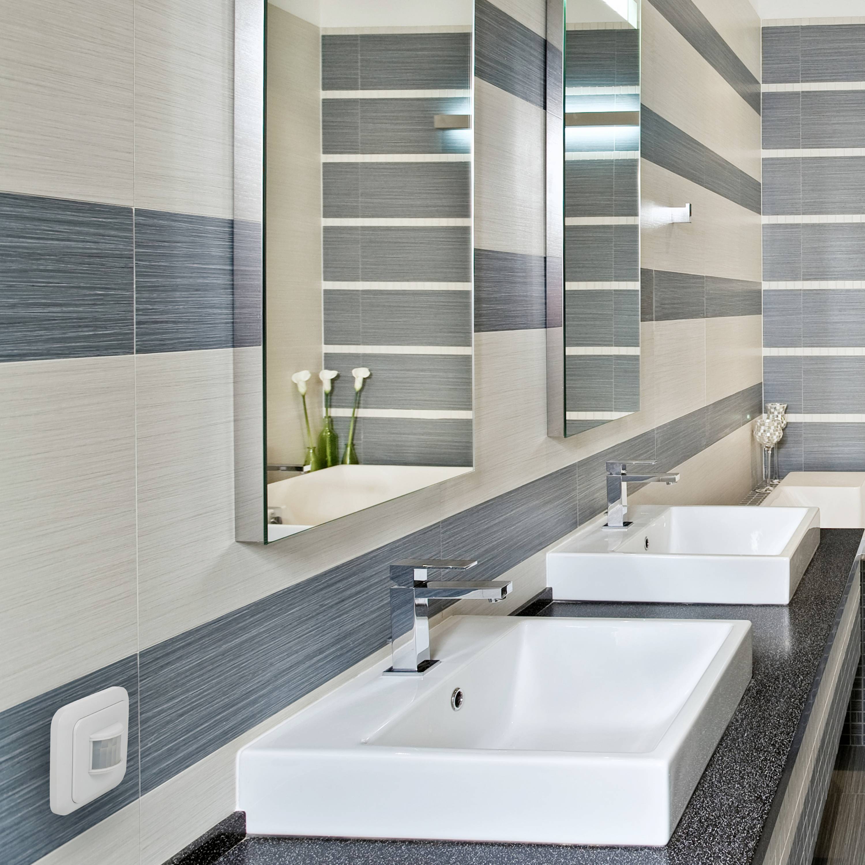 White wash basins with rectangular mirrors in a modern bathroom with striped wall tiles. Two vases with white flowers.