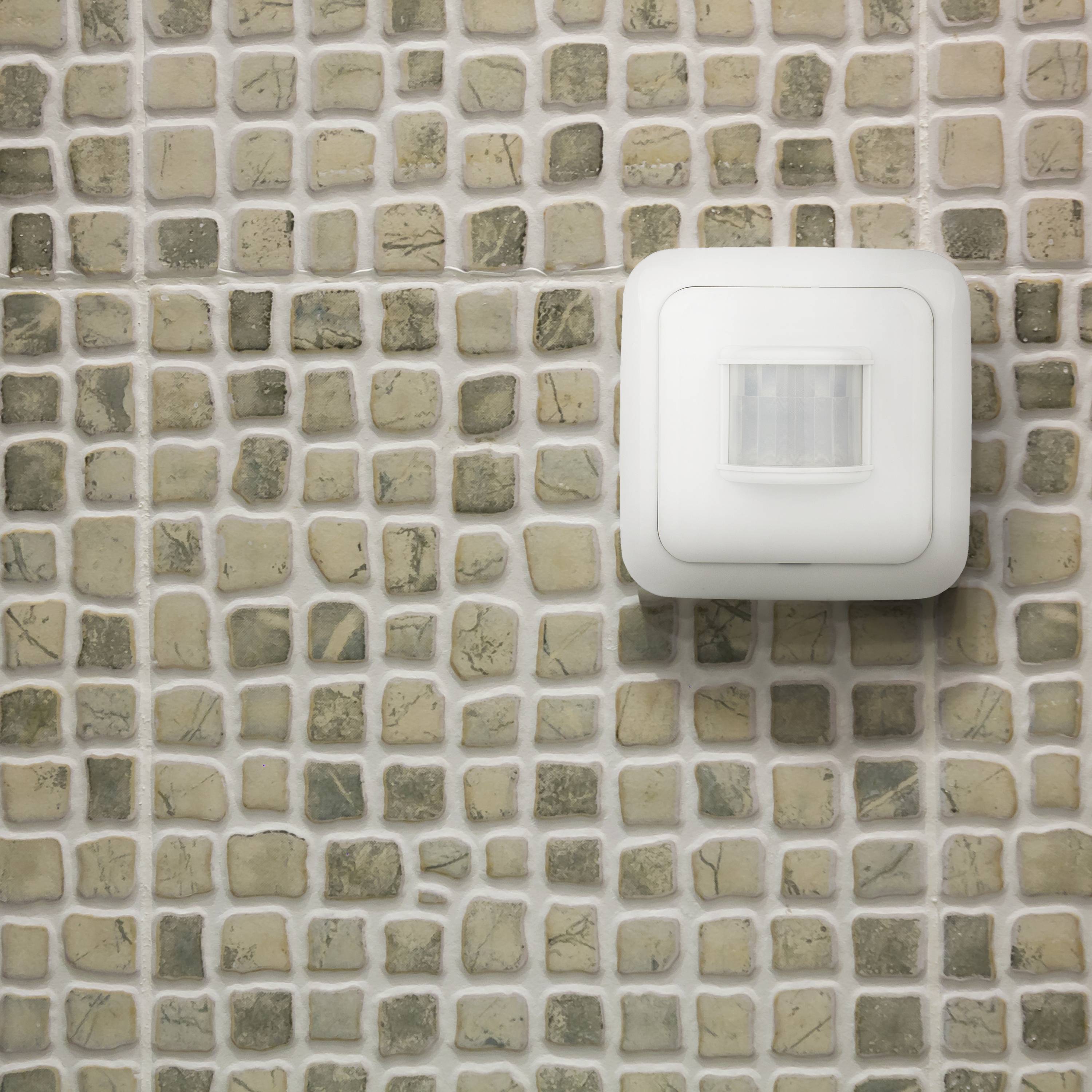 A motion sensor on a wall clad with mosaic tiles.