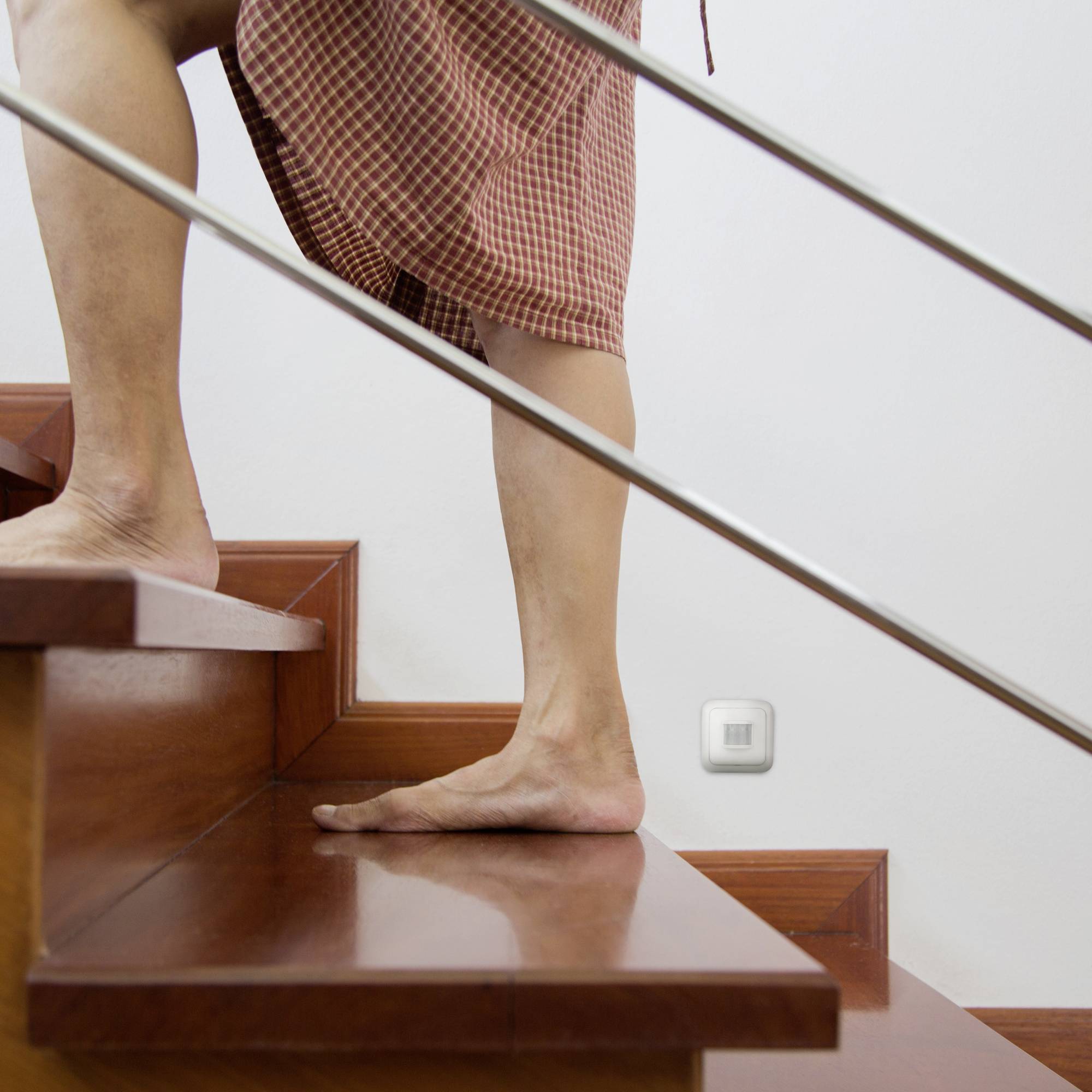 A person in a checked dress is walking barefoot down a wooden staircase.