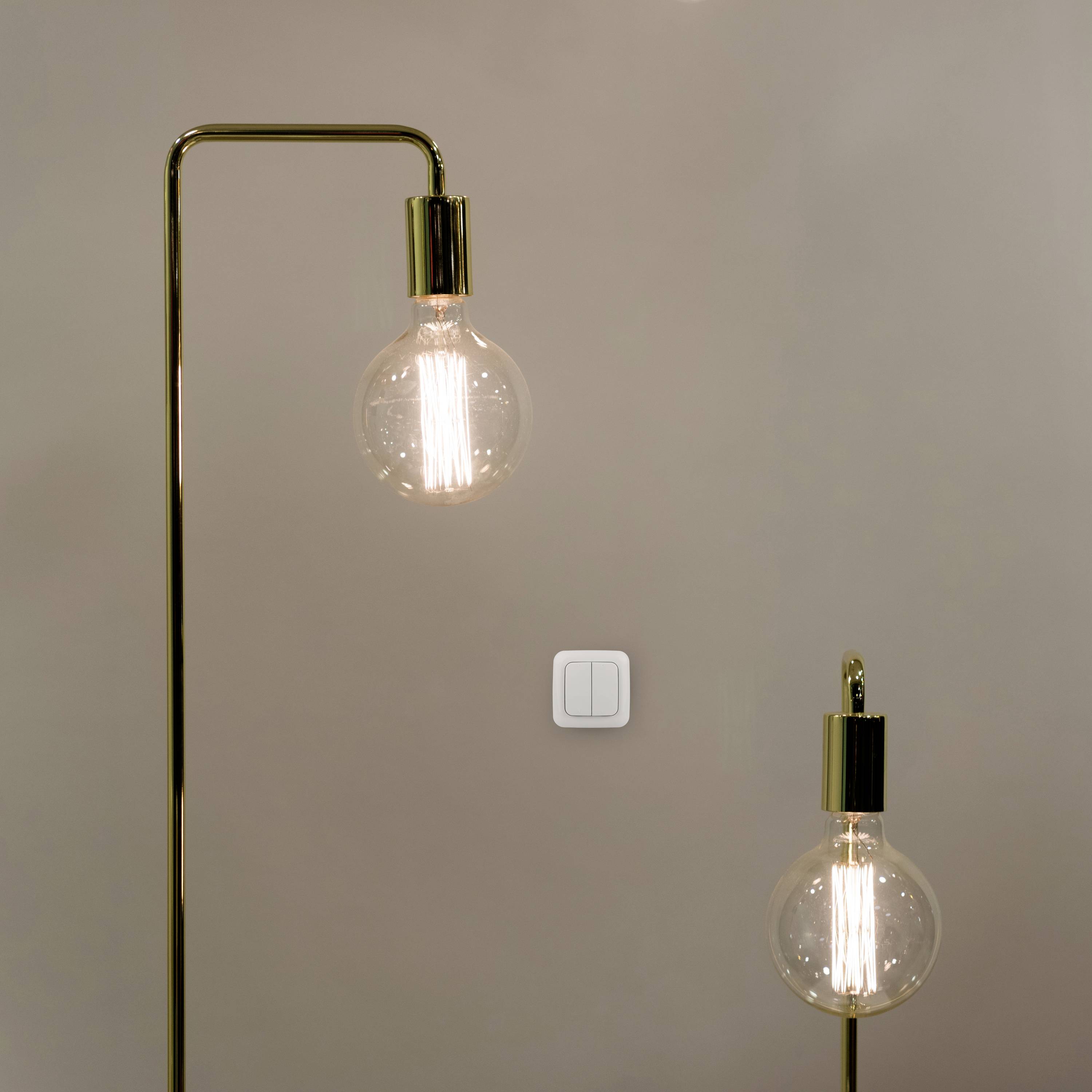 Two standard lamps with simple light bulbs in front of a beige wall, with a light switch visible.