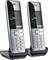 Two cordless telephones stand side by side on their charging stations. They have a modern design and large buttons.