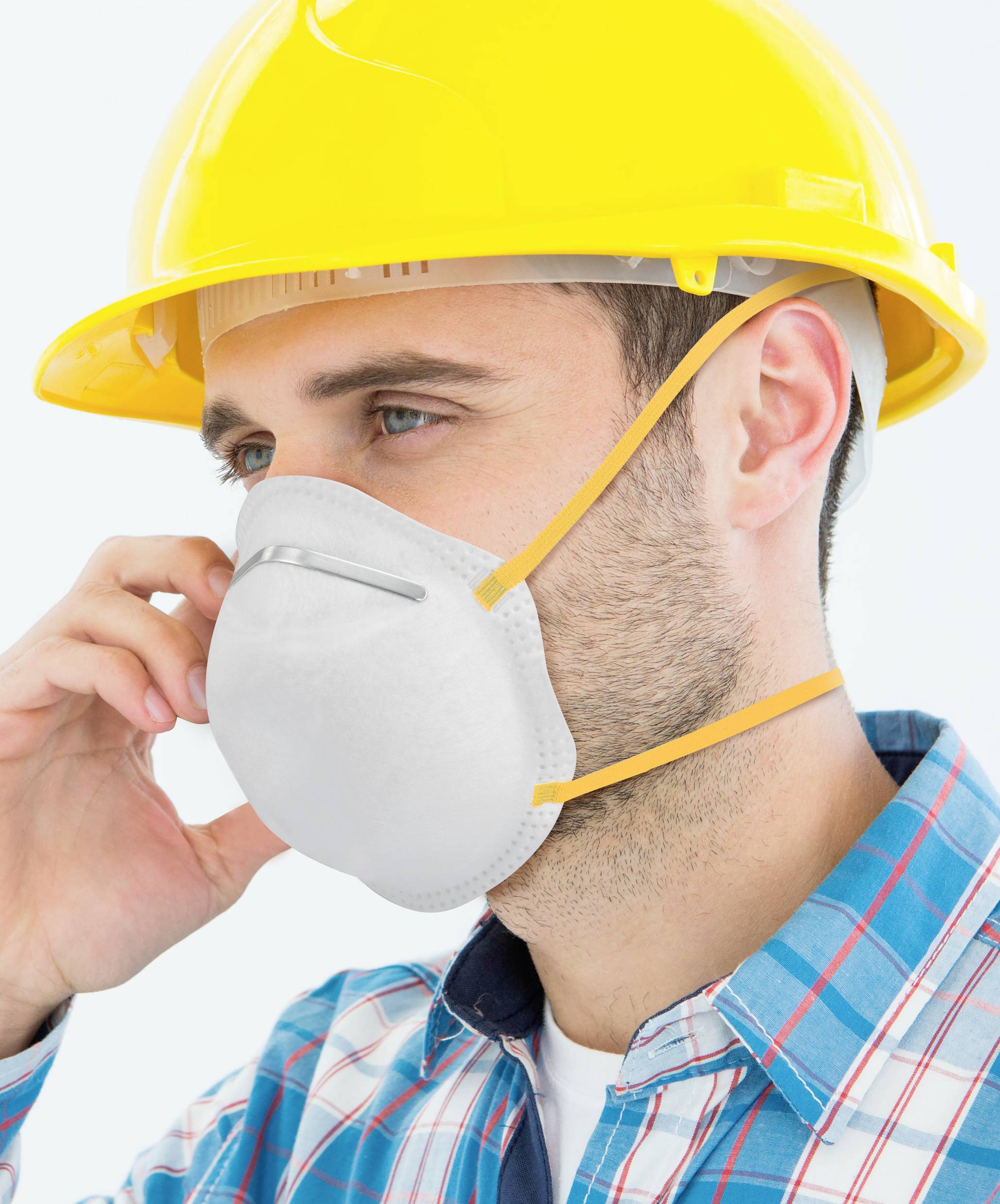 A man is wearing a yellow hard hat and a respiratory mask. He is holding the mask firmly while gazing into the distance.