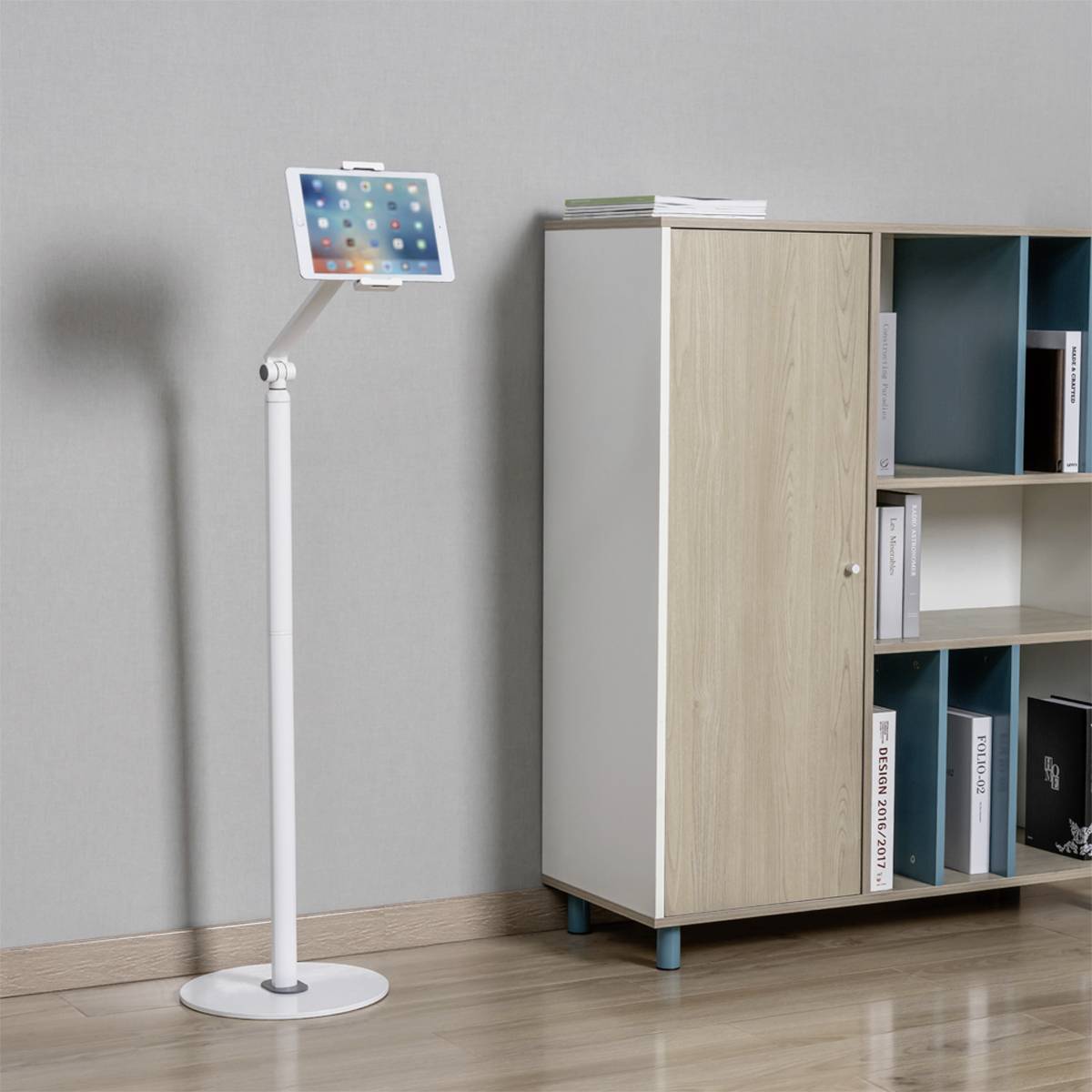 Tablet on a stand next to a bookshelf with books and folders in a bright room.