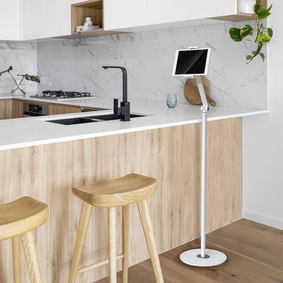 Modern kitchen with a wooden worktop, two bar stools, and a tablet stand. White cupboards, marble splashback, and plants as decoration.