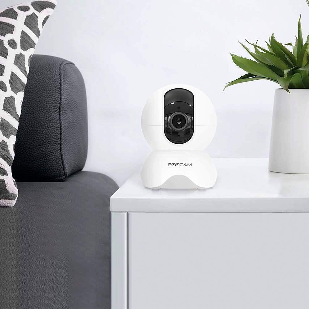 Security camera on a white table next to a grey sofa. The camera is facing towards the room.