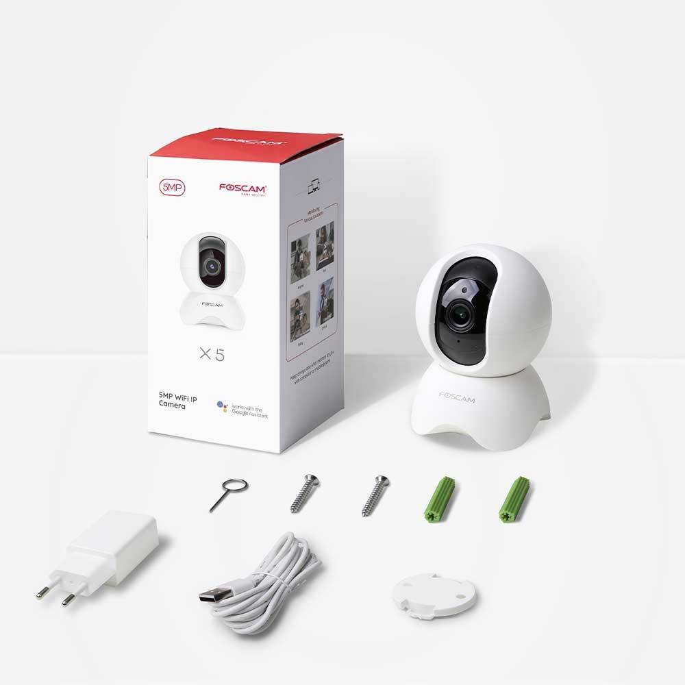A surveillance camera with a white casing and accessories lies next to a red and white product packaging on a table.