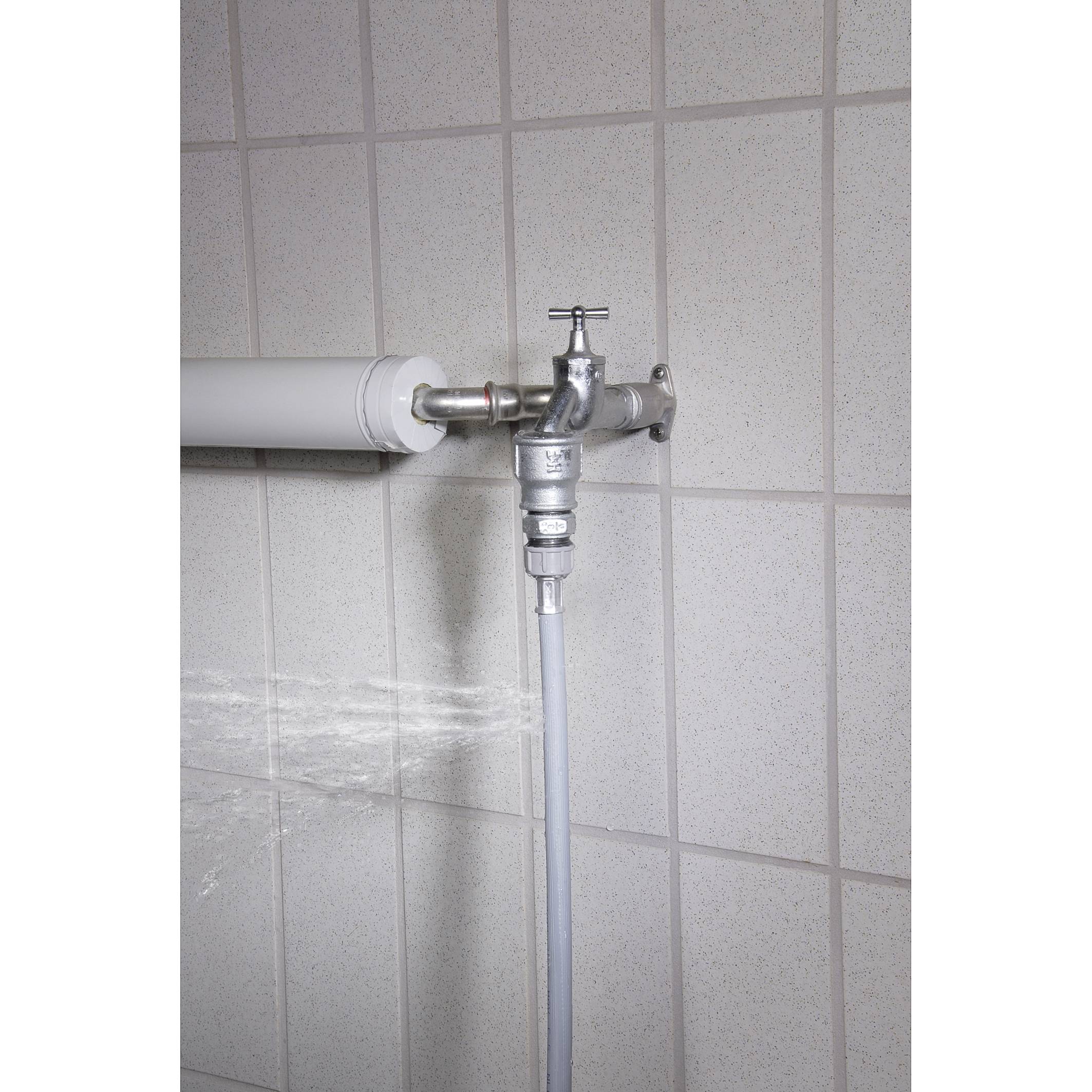 A tap on a tiled wall is open, water is spraying out. An attached hose hangs downwards.
