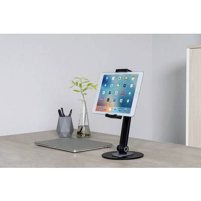 A tablet on a black stand, placed on a desk next to a closed laptop, a vase with plants, and a pencil holder.