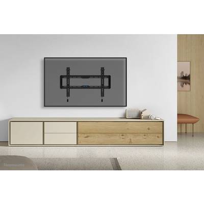 TV wall mount installed on a white wall, in front of a minimalist white-beige TV console with wooden details. A small speaker stands to the left.