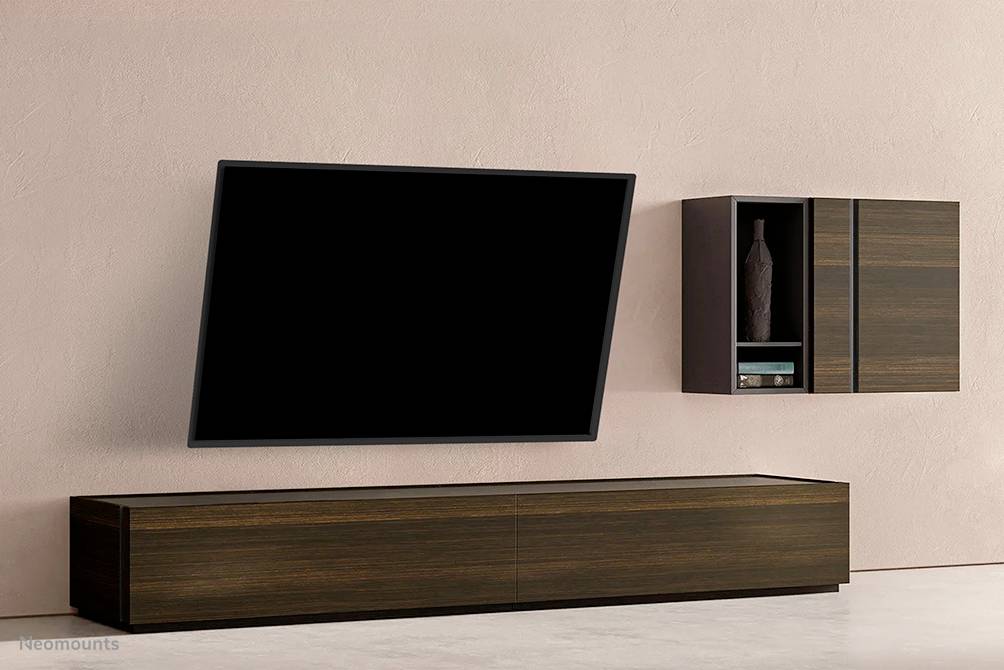 A modern living room setup with a wall-mounted flat-screen television at an angle, with a wooden shelving unit beside it adorned with decorative items.