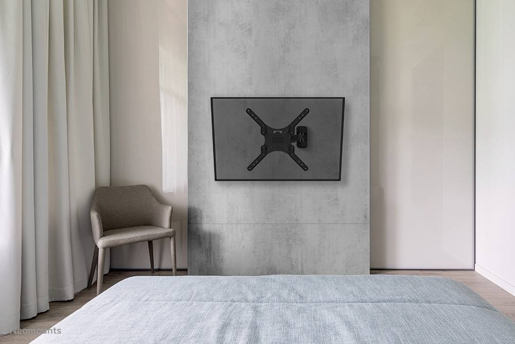 A modern bedroom shows a flat-screen television mounted on the wall, a chair and a bed with a blue duvet.