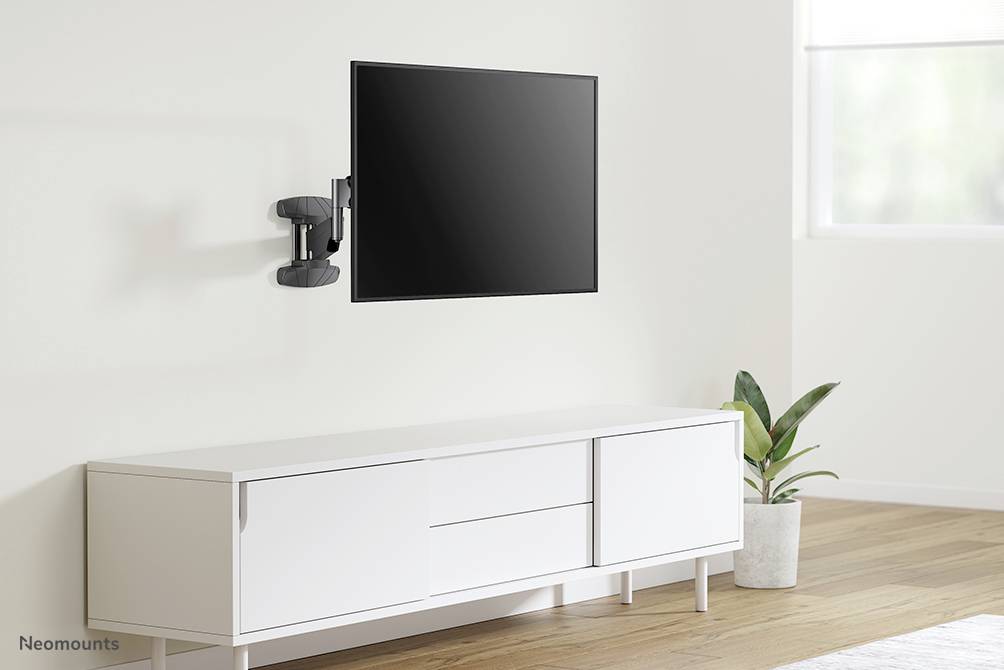 A bright room with a flatscreen television mounted on the wall above a white sideboard. A plant stands beside it.