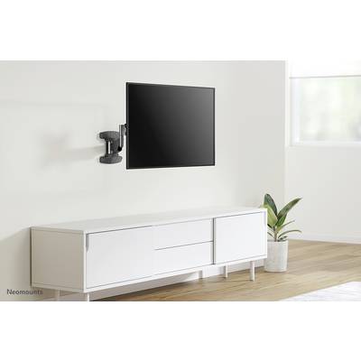 A bright room with a flatscreen television mounted on the wall above a white sideboard. A plant stands beside it.