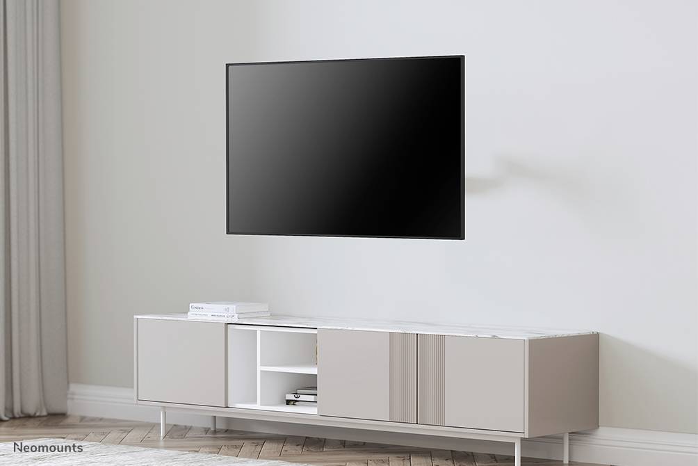 A modern flat-screen television is mounted on a wall above a minimalist, white TV unit in a bright room.