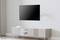 A modern flat-screen television is mounted on a wall above a minimalist, white TV unit in a bright room.