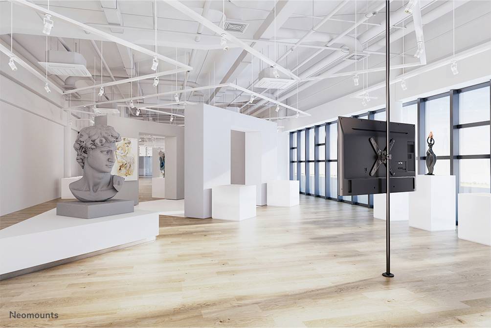 A modern, bright exhibition space with white walls, wooden flooring, a head sculpture, and large windows in the background.