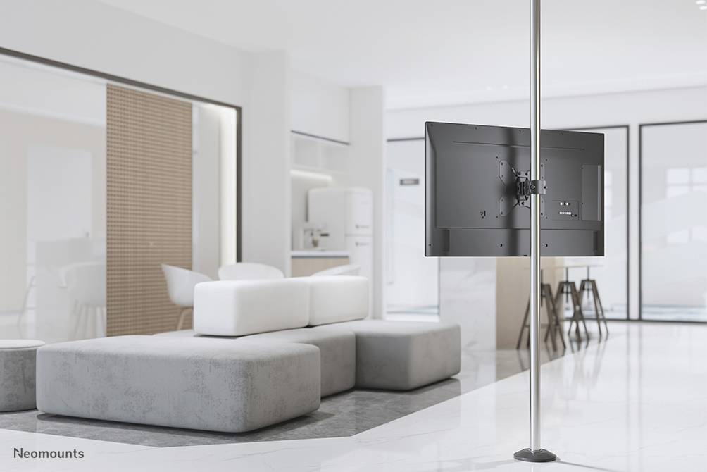 A modern, bright living space with a flat-screen television mounted on a floor-to-ceiling pole. Sofas and a kitchen are visible in the background.
