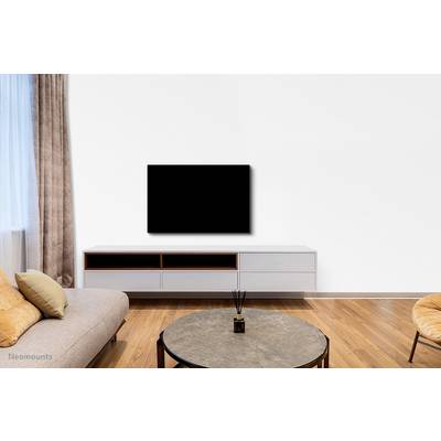 Living room with light wooden flooring, grey sofa, round table, white TV unit and black flat-screen television mounted on the wall.
