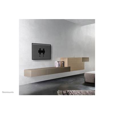 A minimalist living room with a grey wall. A flat television is wall-mounted, with floating shelves beside it displaying books.