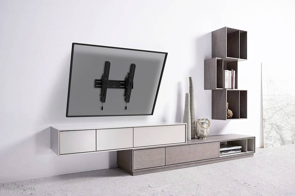 Wall-mounted television with adjustable bracket above a modern white and brown entertainment unit in a stylish, minimalist room.