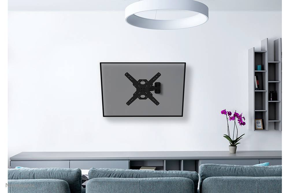 A television mounted on a wall in a modern living room with grey furniture and a flower pot with orchids on a shelf.