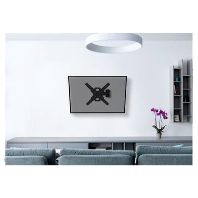 A television mounted on a wall in a modern living room with grey furniture and a flower pot with orchids on a shelf.