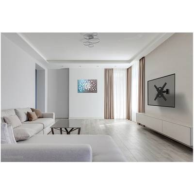 Bright living room with a grey sofa, coffee table, wall decor and TV mount on the wall. Large windows with beige curtains.