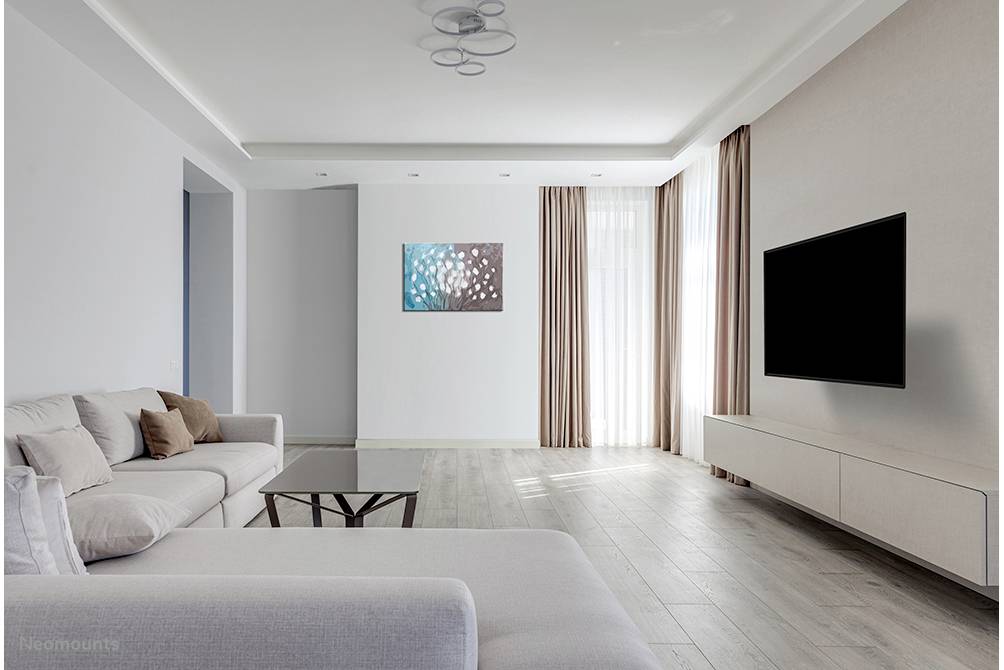 Bright living room with a grey sofa, modern coffee table and large flatscreen television mounted on the wall, with large windows and curtains on the right.