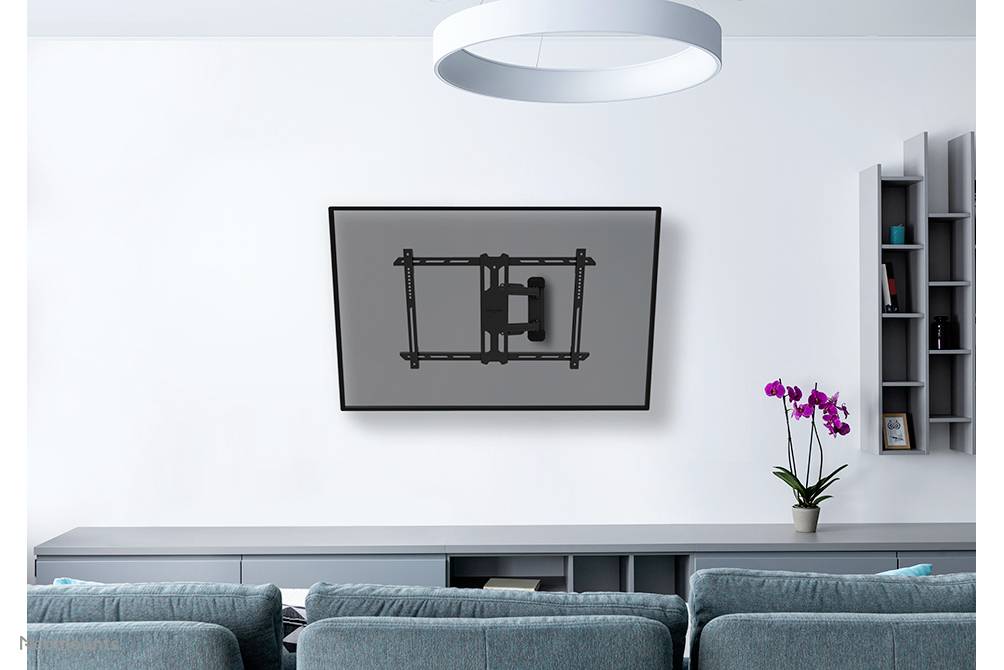 A contemporary living space with a grey sofa in the foreground. A mounted television hangs on the white wall, beside which is a shelf with an orchid.