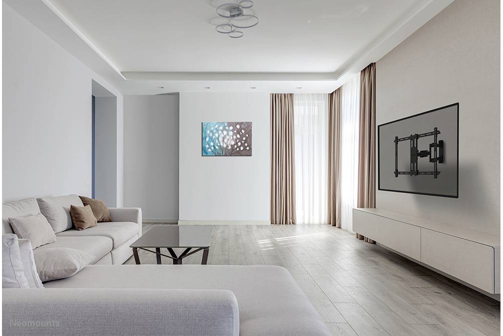 Bright living room with modern furniture: grey sofa, coffee table, wall art and empty wall mounting for TV. Wooden flooring and light curtains.