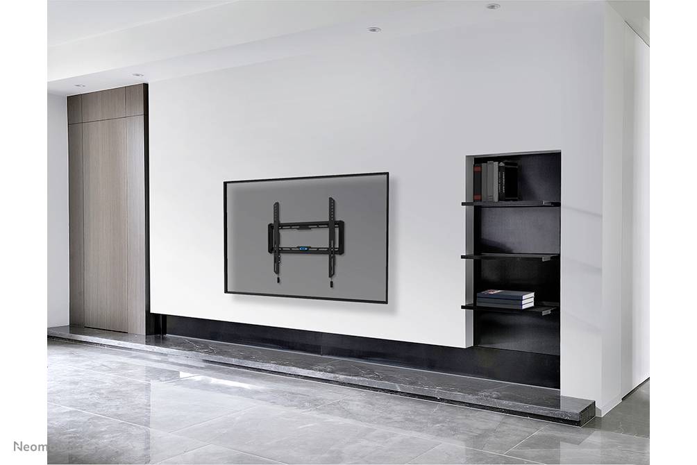 A modern, minimally furnished room with a television mounted flat against the wall and a bookshelf lined with books.