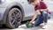 A man is checking the tyre pressure of a car with a portable device. The man is kneeling beside the car and wearing a red T-shirt.