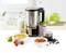 A blender sits on a table, surrounded by a bottle of milk, a bowl of soup, a bowl of sauce, a glass with berries and chickpeas.