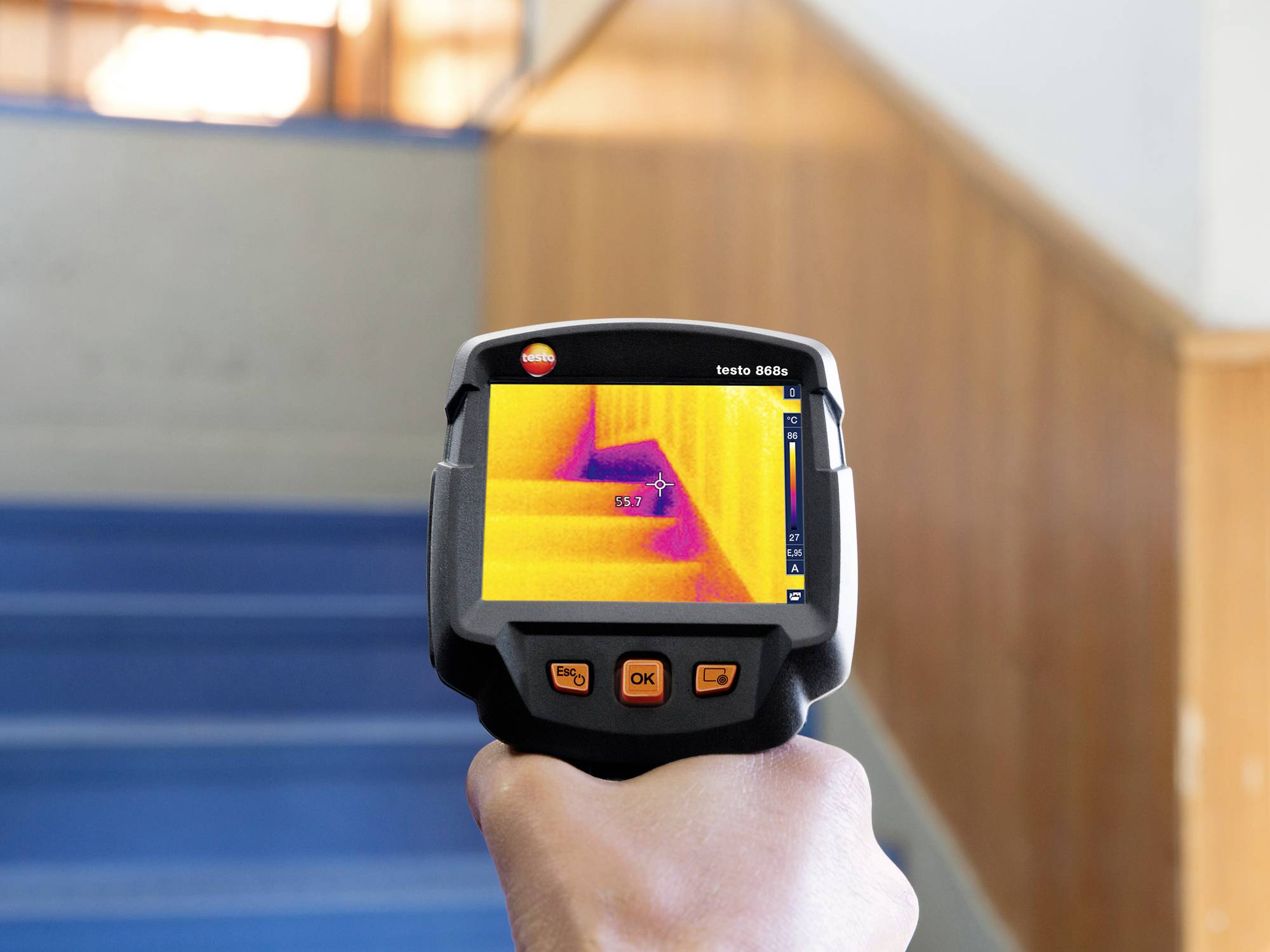 A person is holding a thermal imaging camera pointed at stairs. The screen displays temperature variations across the steps.