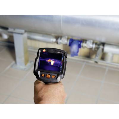 A hand holds a thermal imaging camera scanning pipelines. The display shows temperature variations to detect potential leaks.