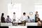 A group of eight people are chatting in a modern office with large windows. Some are standing, others are sitting relaxed.