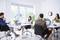 Several people are working in a modern office with laptops and desks, surrounded by plants and large windows.
