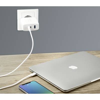A smartphone and a laptop are lying on a table. Both are connected to a charger plugged into a wall socket.