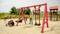 Playground scene with children playing on a swing, with a wheelchair-accessible entrance clearly visible. A climbing frame and trees can be seen in the background.