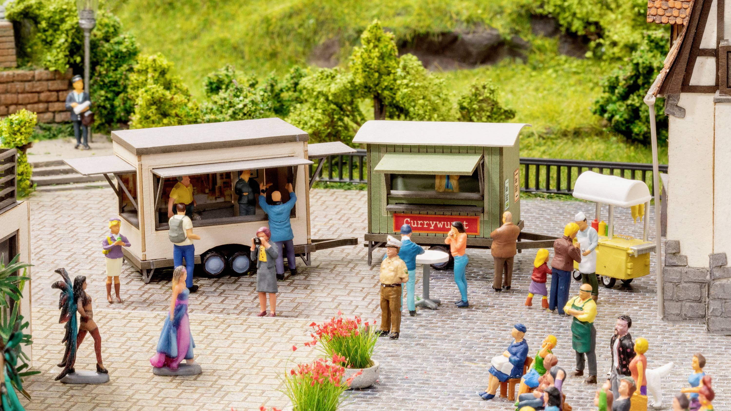 A miniature village scene with market stalls where people are interacting. A green landscape is visible in the background.