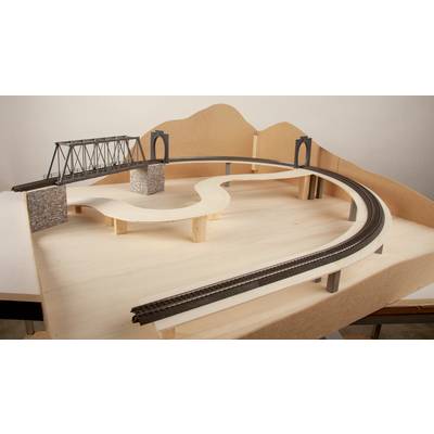 Model railway landscape under construction with a bridge and curved track, on a wooden base, without decorative elements.